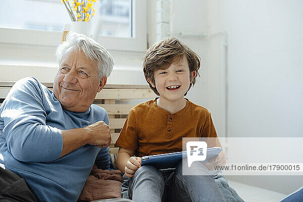 Happy boy with tablet PC sitting by grandfather at home