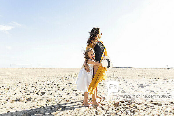 Mature woman with daughter standing at beach on sunny day