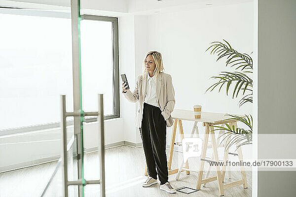 Businesswoman standing in modern office using mobile phone