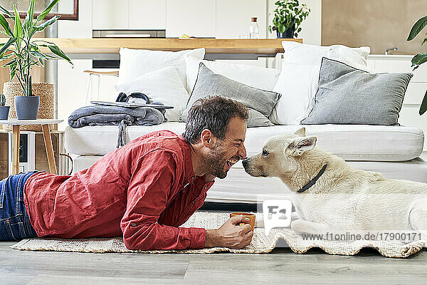 Happy man with coffee cup lying with dog at home