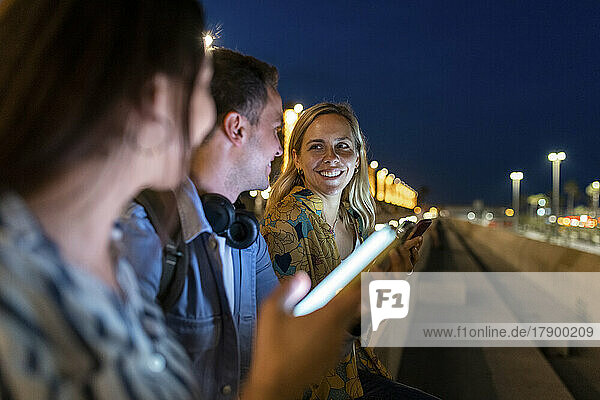 Happy woman talking with friends holding smart phones at night