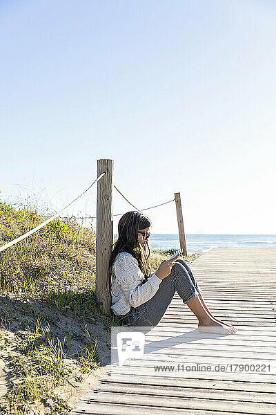 Girl reading book sitting on boardwalk at beach