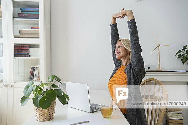 Smiling freelancer stretching arms at desk in home office