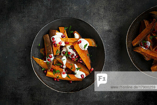 Studioaufnahme von zwei Schüsseln Süßkartoffeln mit Petersilie  Granatapfelkernen und Joghurtsauce