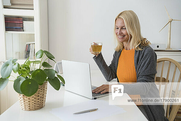 Happy freelancer with tea cup working on laptop at home office