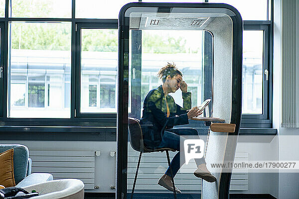 Businesswoman working on tablet computer sitting in soundproof cabin