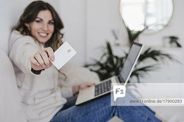 Smiling young woman with laptop showing credit card