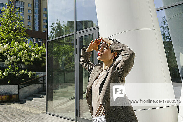Businesswoman shielding eyes standing in front of column