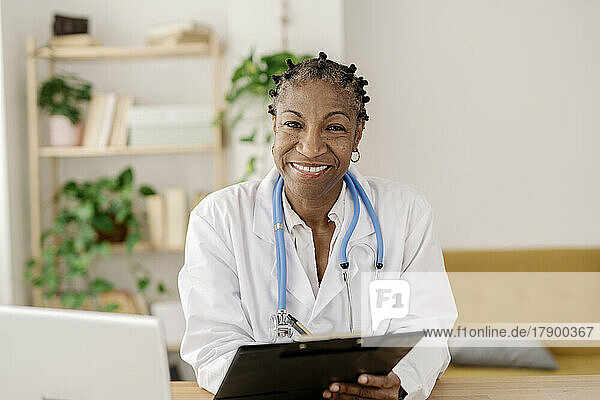 Happy doctor with clipboard sitting at home office