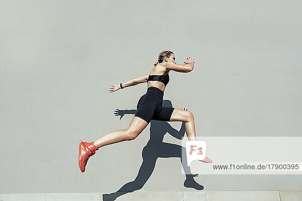 Young athlete jumping by gray wall on sunny day