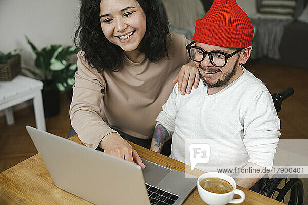 Cheerful woman using laptop sitting by boyfriend with disability at home