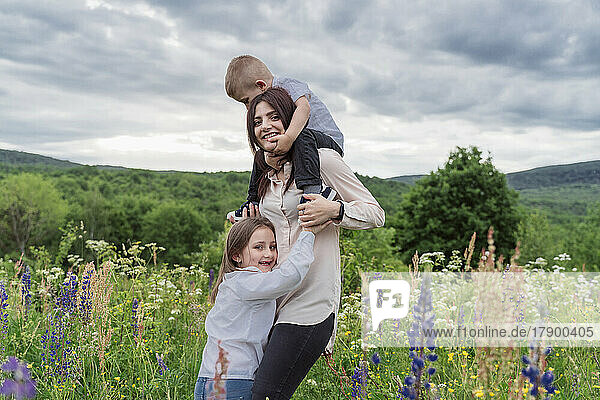 Playful mother with children in lupine flowers meadow