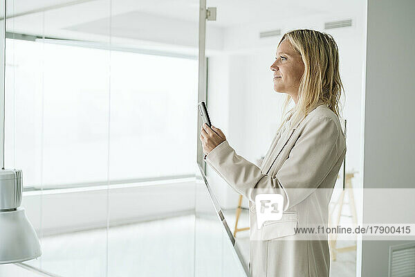 Businesswoman holding mobile phone in minimalist office corridor