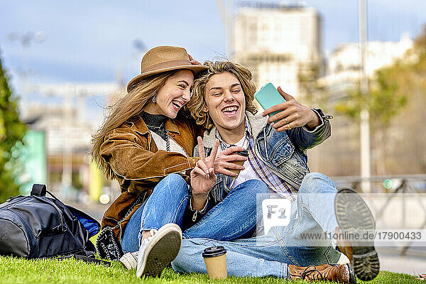 Happy tourist couple taking selfie through smart phone sitting in park
