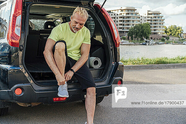 Mann sitzt im Kofferraum eines Autos und bindet Schnürsenkel
