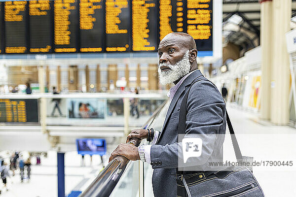 Thoughtful senior businessman with laptop bag at railroad station