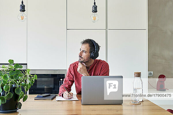 Thoughtful freelancer sitting with laptop at home