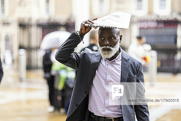 Senior businessman covering head with newspaper on rainy day