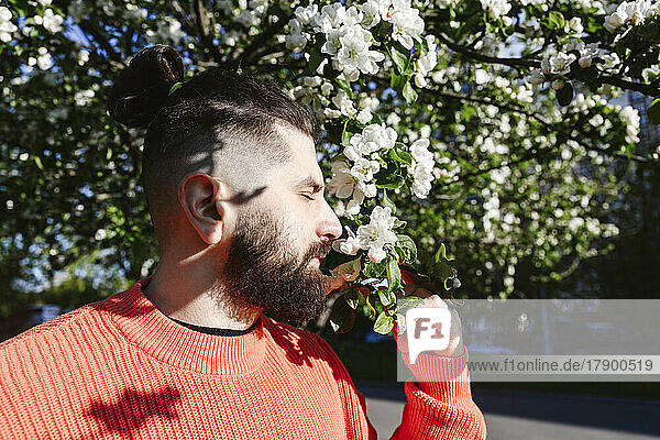 Man with eyes closed smelling white flower