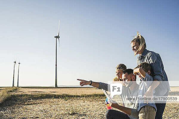 Family using digital tablet in wind park pointing at wind turbines