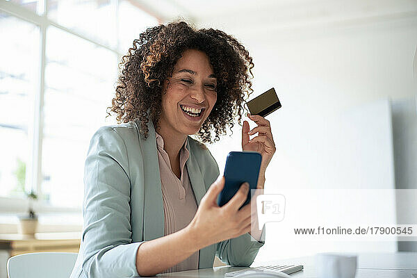 Happy businesswoman doing online payment through smart phone at workplace