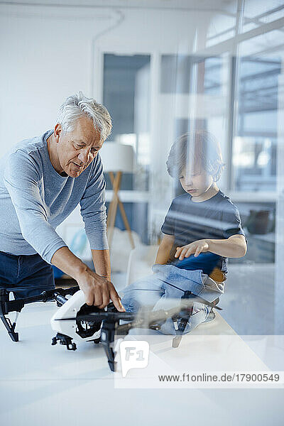 Senior man examining drone by grandson at home