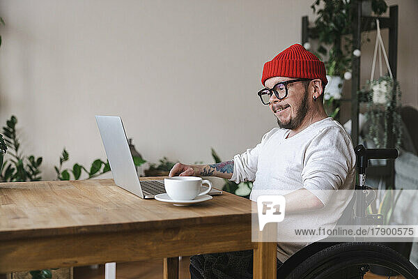 Smiling man in wheelchair using laptop at home