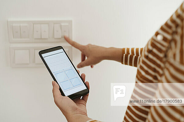 Woman touching switch for blinds while checking mobile phone app