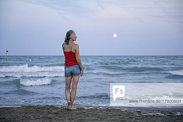 Frau steht am Strand mit Mond über dem Horizont