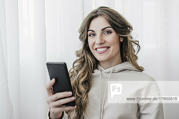Lächelnde junge Frau mit Mobiltelefon zu Hause