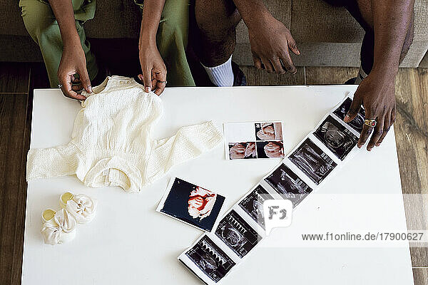 Couple with baby clothing and ultrasound pictures on table