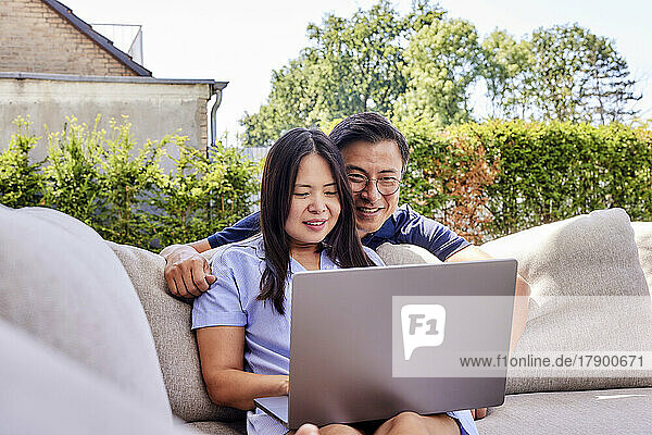 Smiling freelancers sharing laptop on sofa