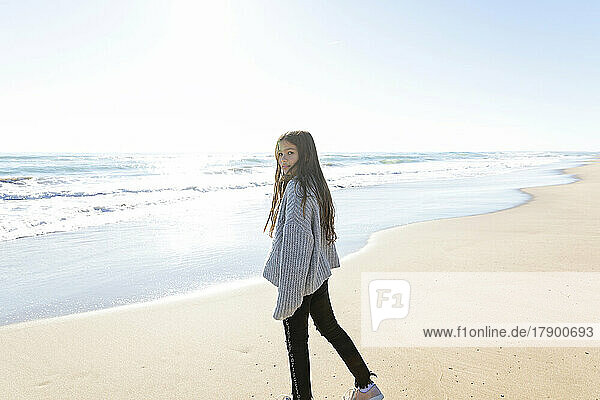 Girl wearing sweater standing at beach on sunny day