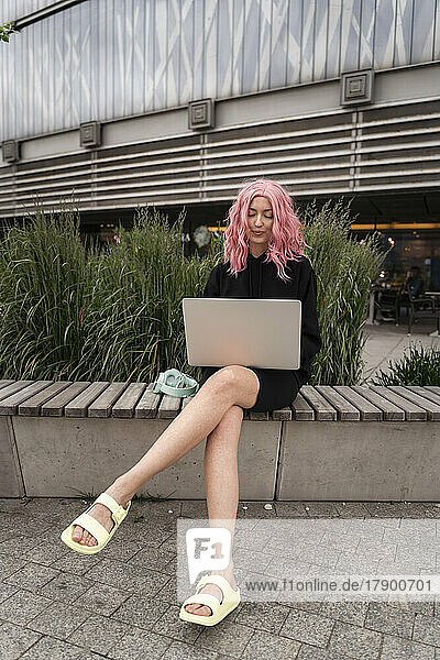 Frau mit rosa Haaren sitzt mit Laptop auf Bank