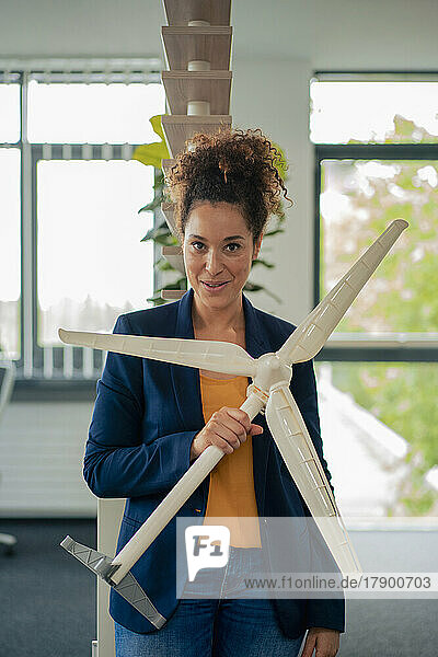 Selbstbewusste Geschäftsfrau mit Windturbinenmodell am Arbeitsplatz