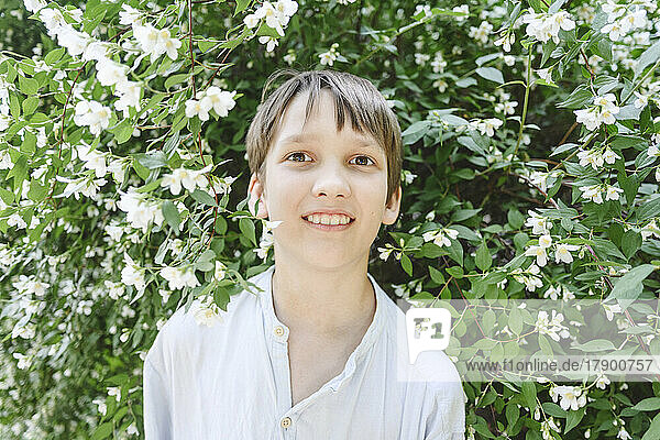 Smiling boy standing amidst plants with jasmine flowers