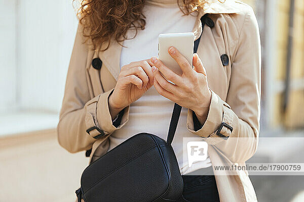 Woman wearing coat text messaging through smart phone