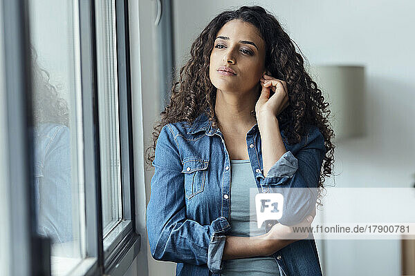 Beautiful woman with curly hair standing by window at home