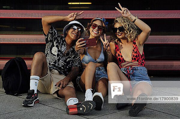 Young friends taking selfie through smart phone sitting in front of shutter