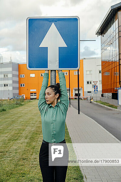 Businesswoman with arms raised holding arrow sign board on footpath