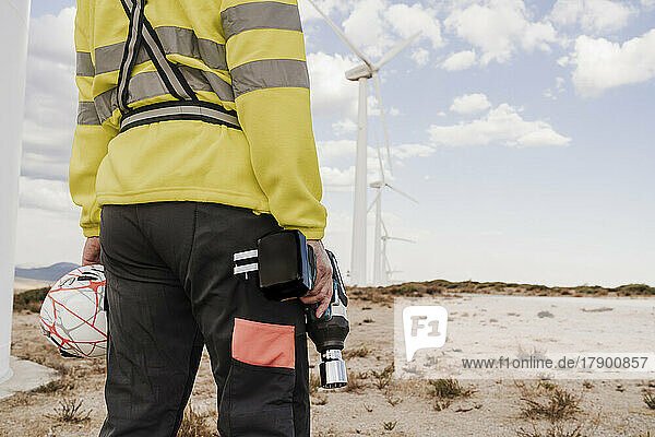 Technician with work tool and helmet standing at wind farm
