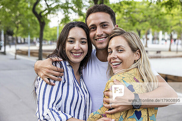 Smiling young man with arms around women at park
