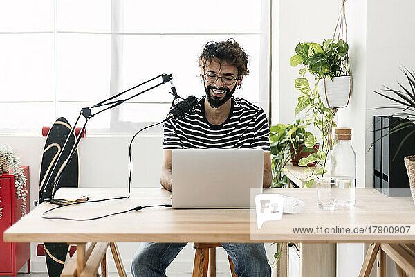 Happy man with microphone and laptop recording podcast in home studio