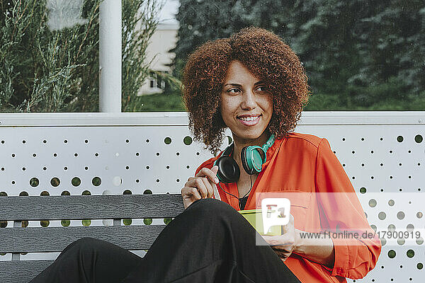 Lächelnde Frau sitzt mit Lunchbox auf der Bank