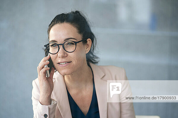 Businesswoman talking on mobile phone in front of gray wall seen through glass