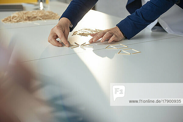 Hände einer Geschäftsfrau  die ein Hausmodell mit Stöcken auf dem Tisch herstellt