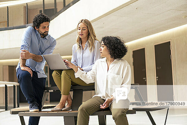 Geschäftsfrau diskutiert am Laptop mit Kollegen im Büroflur
