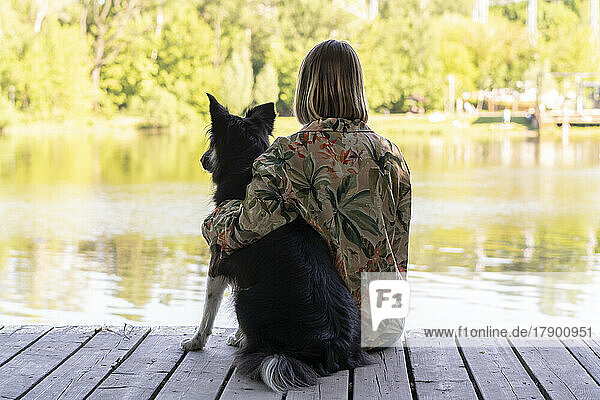 Young woman sitting with dog by lake at park