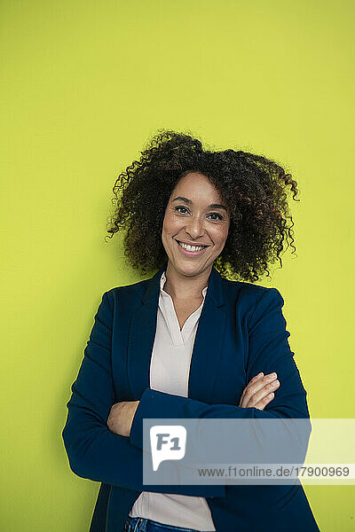 Smiling businesswoman with arms crossed in front of green wall