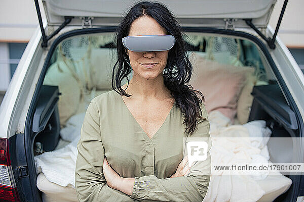 Smiling woman wearing virtual reality simulator in front of car trunk